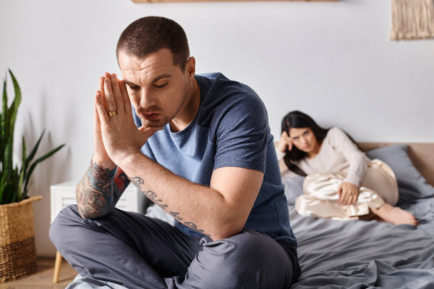 young depressed tattooed man sitting on bed near offended asian wife, family divorce concept - Photo, Image