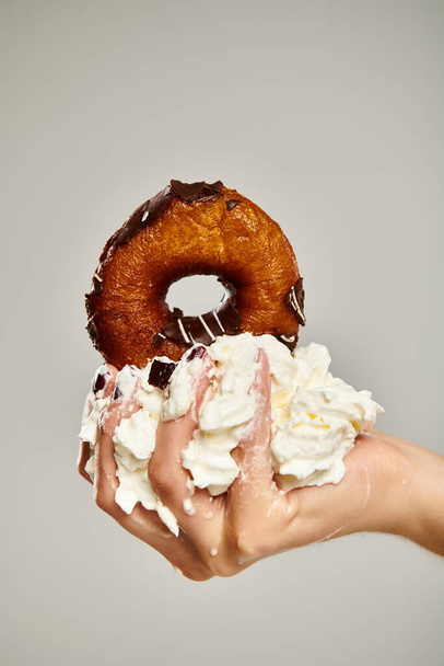 object photo of delicious donut with brown icing and whipped cream in hand of young unknown woman - Photo, Image