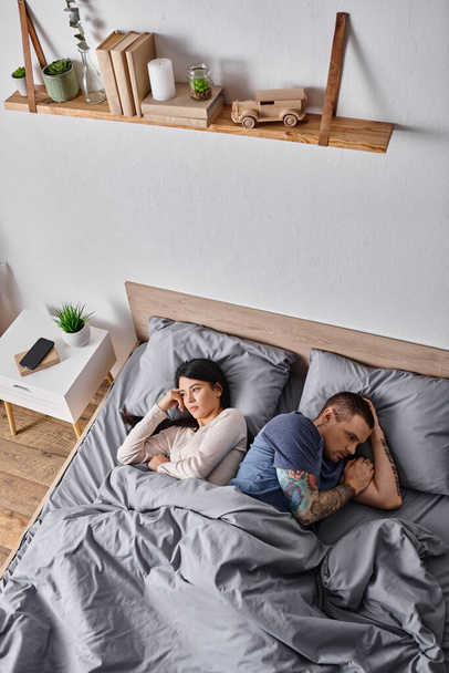wysoki kąt widzenia sfrustrowanej wielokulturowej pary leżącej na łóżku w domu, problemy rodzinne - Zdjęcie, obraz