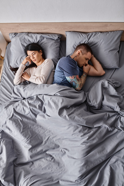 high angle view of depressed interracial couple lying down on bed at home, family divorce concept - Photo, Image