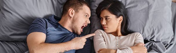 rozzlobený multikulturní pár ležící na posteli, křičící a hádající se na sebe, pohled shora, prapor - Fotografie, Obrázek