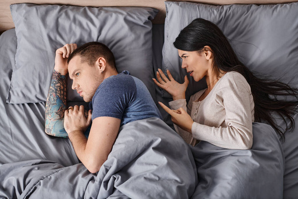 怒っているアジアの女性のトップビュー ベッドに横たわるタトゥーの若い夫,離婚 - 写真・画像