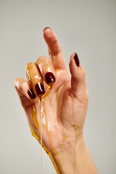 mano de señora desconocida apuntando hacia arriba mientras está cubierto con miel deliciosa orgánica sobre fondo gris - Foto, imagen