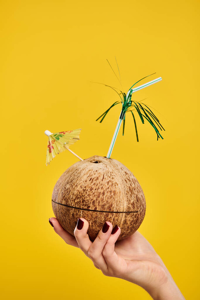 object photo of cocktail in fresh coconut decorated with umbrella in hand of unknown woman - Photo, Image