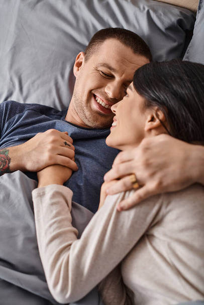vue de dessus de jeune et joyeux couple interracial embrassant dans la chambre à coucher à la maison, bonheur familial - Photo, image