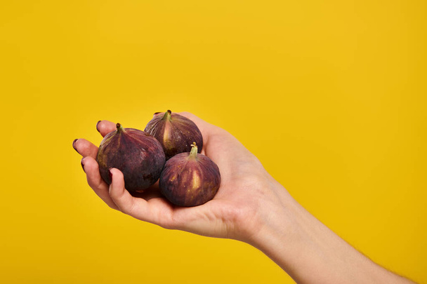 object photo of delicious organic figs in hand of young unknwon woman on vibrant yellow backdrop - Photo, Image