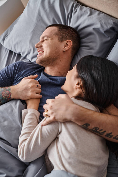 vista superior de jovem casal interracial alegre abraçando no quarto em casa, felicidade familiar - Foto, Imagem