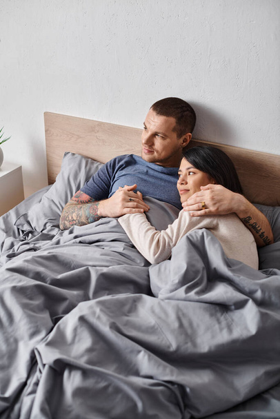 junges glückliches multiethnisches Paar, das sich zu Hause im Bett umarmt und die Hände hält, Harmonie und Zärtlichkeit - Foto, Bild