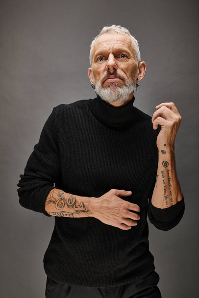 attractive fashionable mature man with beard in chic black turtleneck posing and looking at camera - Photo, Image