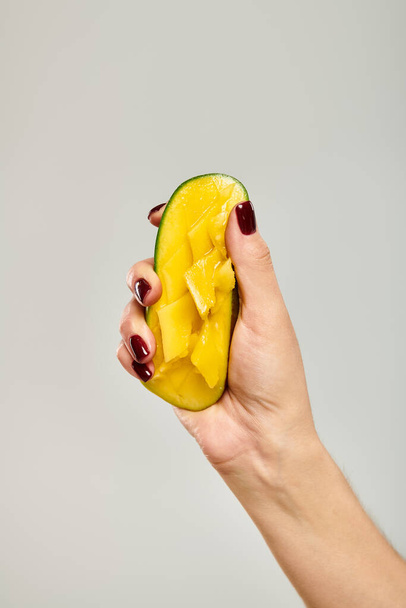 unknown young female model squeezing juicy sweet mango in her hand while on gray background - Photo, Image