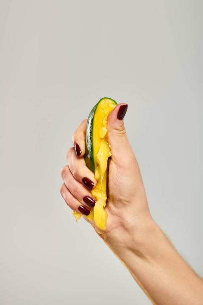 onbekend jong vrouwelijk model met nagellak knijpen verse mango in haar hand op grijze achtergrond - Foto, afbeelding