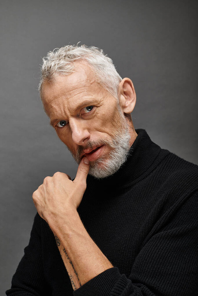 appealing fashionable mature man with beard in trendy black turtleneck posing and looking at camera - Photo, Image