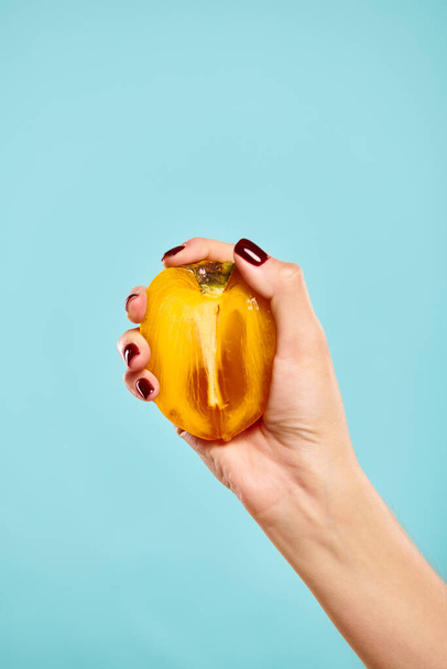 objekti kuva herkullisia tuoreita persimmon kädessä tuntematon nainen kynsilakka sinisellä taustalla - Valokuva, kuva