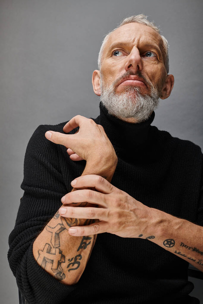 handsome mature male fashionista with gray beard in chic black turtleneck posing and looking away - Zdjęcie, obraz