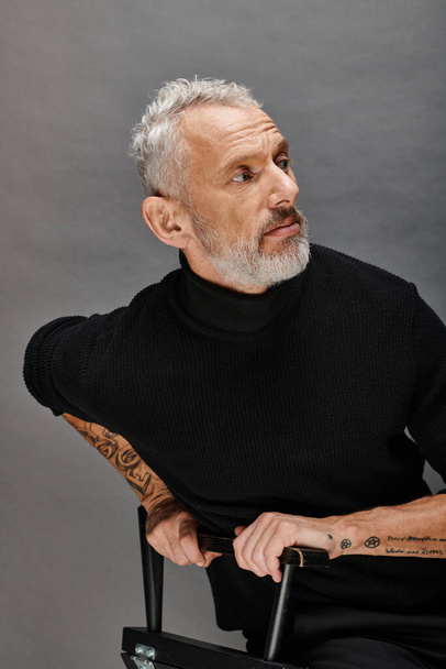 appealing mature male model in fashionable turtleneck sitting on folding chair and looking away - Photo, Image