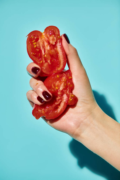 red delicious gourmet pieces of fresh tomato squeezed by unknown female model on vivid background - Photo, Image