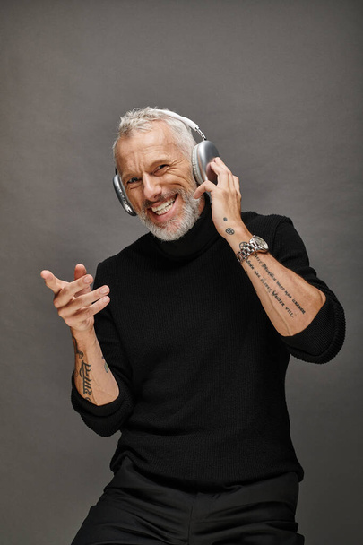 cheerful handsome mature man in stylish black turtleneck with modern headphones looking at camera - Photo, Image