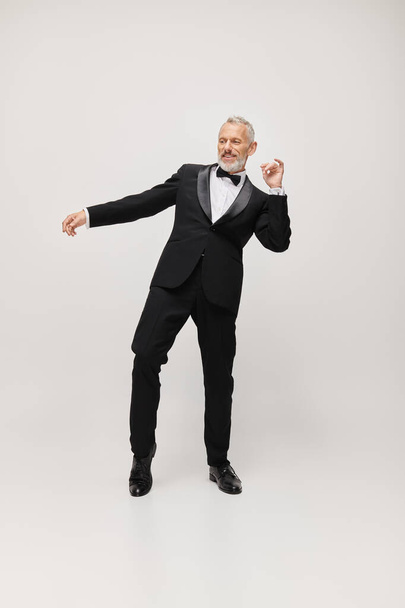 attrayant homme mature heureux avec barbe grise et noeud papillon dans élégant smoking dansant activement - Photo, image