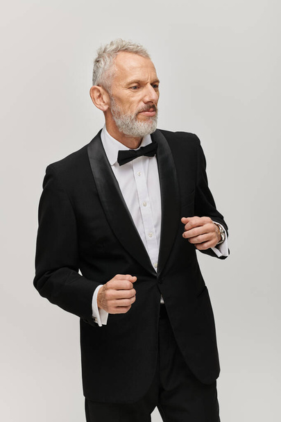 attractive bearded mature man in debonair black tuxedo with bow tie posing in motion while dancing - Fotó, kép