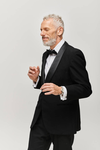 attractive bearded mature man in debonair black tuxedo with bow tie posing in motion while dancing - Fotó, kép