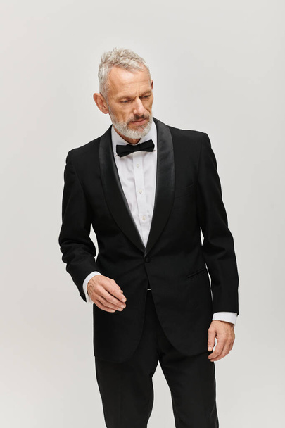 good looking bearded mature man in elegant black tuxedo with bow tie posing and looking away - Fotografie, Obrázek