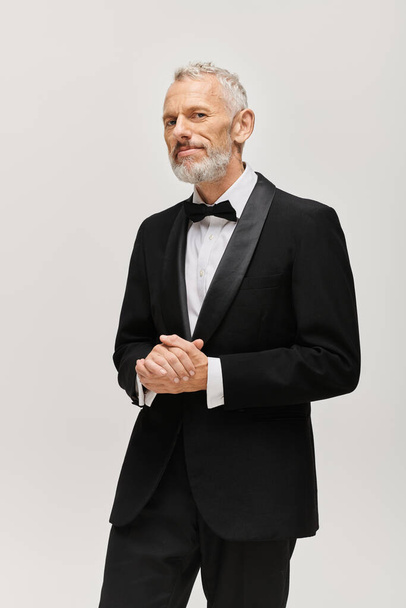 good looking mature bearded man with bow tie in elegant tuxedo posing and looking at camera - Fotografie, Obrázek