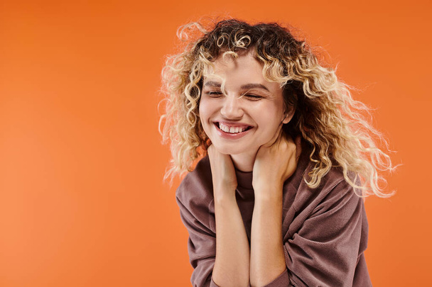 trendikäs nainen aaltoileva hiukset mokka väri poolopaita hymyillen suljetuin silmin oranssi tausta - Valokuva, kuva