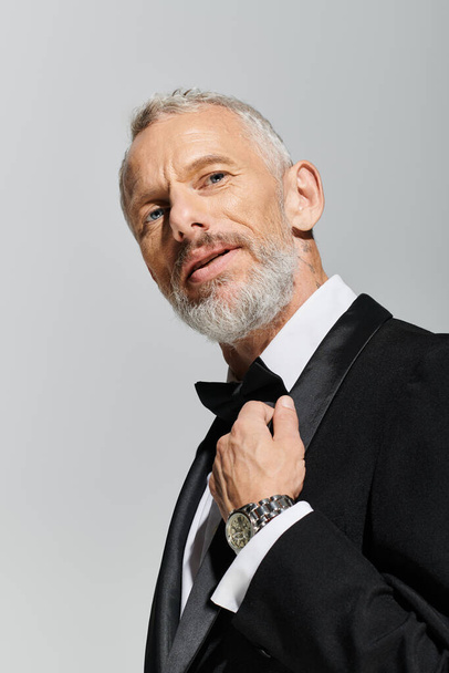 good looking elegant mature man with beard wearing fashionable tuxedo and looking at camera - Photo, Image