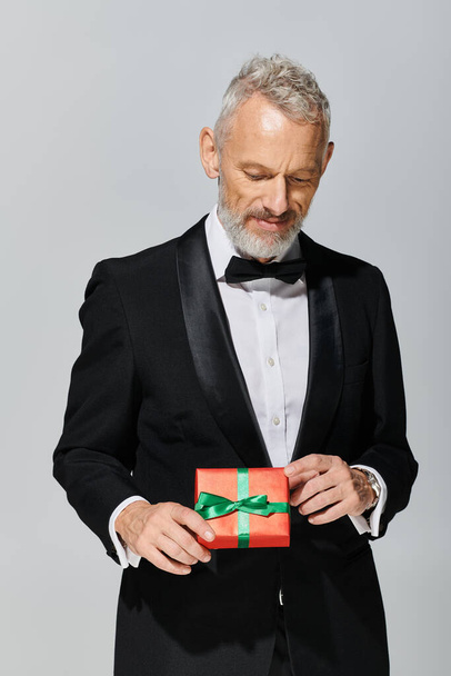 buen aspecto elegante modelo masculino maduro con barba y pajarita en esmoquin mirando regalo en sus manos - Foto, imagen