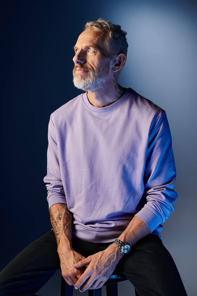 красивый бородатый взрослый мужчина в повседневной фиолетовой толстовке с аксессуарами улыбается и смотрит в сторону - Фото, изображение