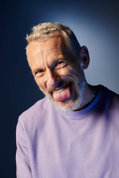 cheerful mature man with gray beard and casual trendy attire grimacing and looking at camera - Photo, Image