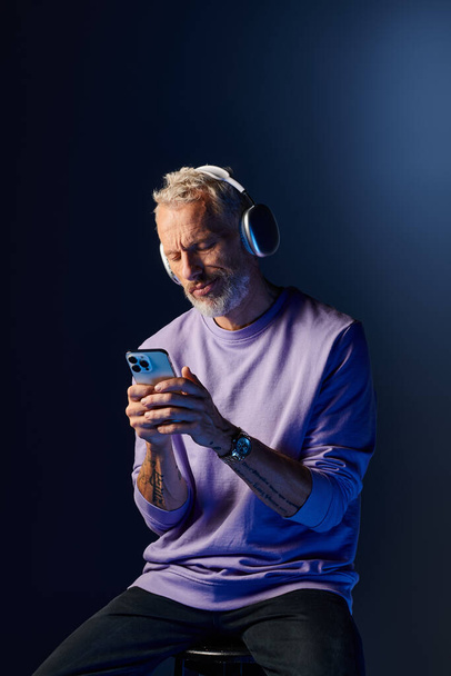 彼のスマートフォンを見ているヘッドフォンと紫色のスウェットシャツの良い見た目成熟した男 - 写真・画像