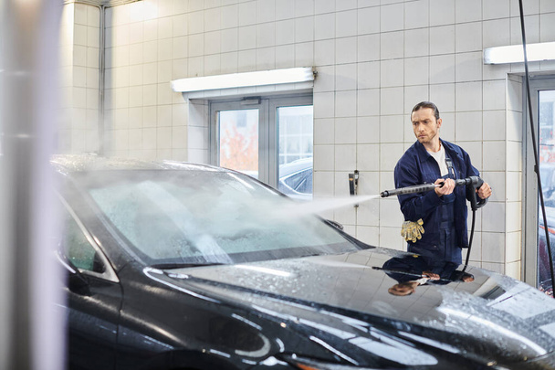 good looking dedicated serviceman with collected hair in uniform washing black car while in garage - Photo, Image