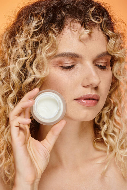 close up portrait of curly woman with perfect skin showing jar of cosmetic cream in studio - Foto, immagini