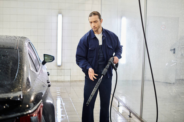 przystojny ciężko pracujący specjalista w mundurze z zebranymi włosami mycie czarny samochód w garażu - Zdjęcie, obraz