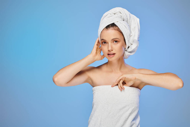 attractive woman with perfect skin and towel on head looking at camera on blue backdrop, wellness - Photo, Image