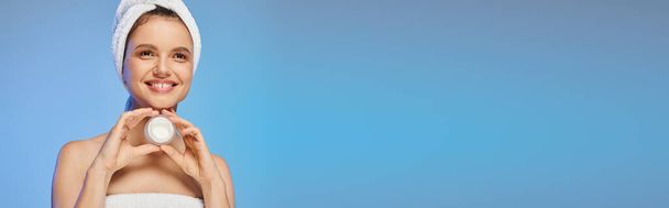 hilpeä nainen pyyhe päässä tilalla purkki kasvovoide sinisellä taustalla, vaakasuora banneri - Valokuva, kuva