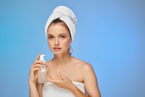 atrakcyjna kobieta z ręcznikiem na głowie i idealnym dozownikiem do twarzy z pianką kosmetyczną na niebiesko - Zdjęcie, obraz