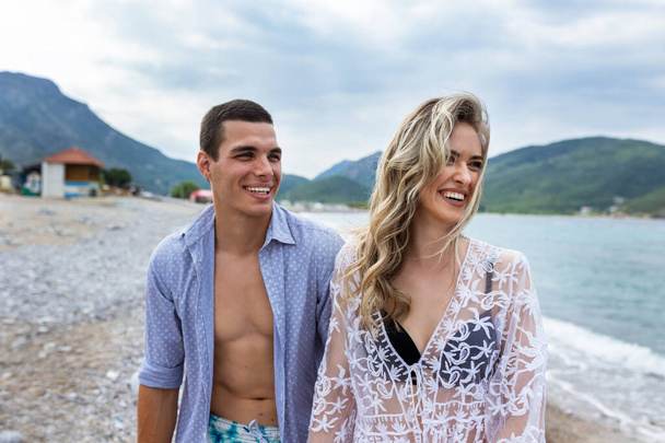 Mutlu genç çift sahilde gülüyor ve el ele tutuşuyor. - Fotoğraf, Görsel