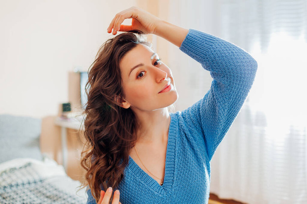 Portrait de jeune femme vérifie ses cheveux après boucleur de cheveux sans chaleur à la maison. Produits de beauté pour coiffure ondulée. - Photo, image