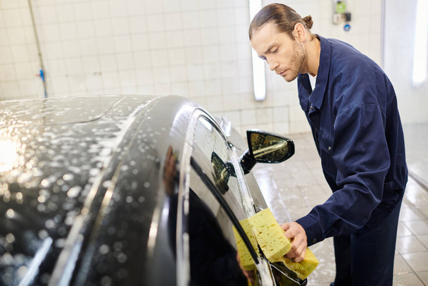 atrakcyjny ciężko pracujący żołnierz w niebieskim mundurze myjący samochód z mydlaną gąbką w garażu - Zdjęcie, obraz