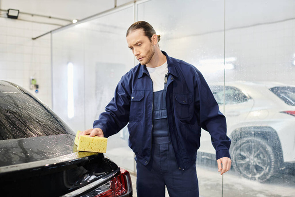 appealing enthusiastic serviceman in blue uniform with collected hair washing car with sponge - Photo, Image