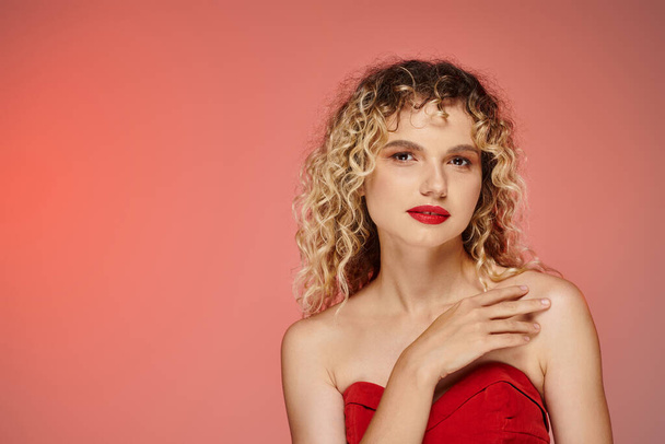 sensual curly woman with bold makeup in red top looking at camera on pink and yellow backdrop - Photo, Image