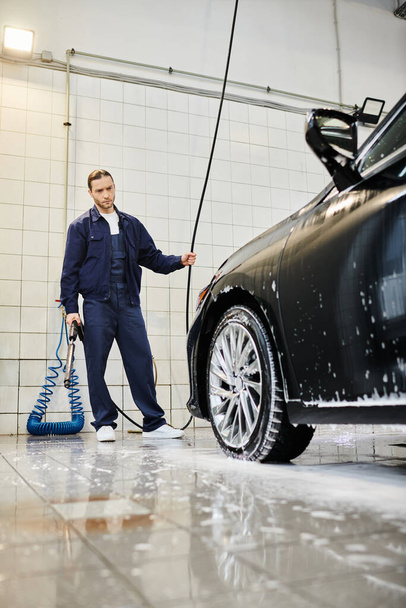 attractive enthusiastic serviceman with collected hair in blue uniform washing modern car using hose - Photo, Image