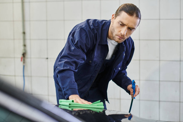 handsome dedicated professional serviceman with collected hair using rag to clean black car - Photo, Image