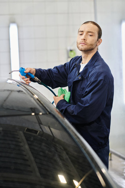 atrakcyjny oddany profesjonalista z zebranym samochodem do mycia włosów z wężem i szmatą w garażu - Zdjęcie, obraz