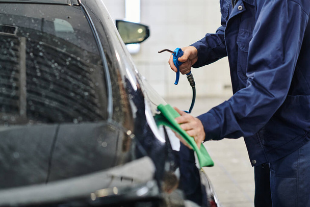 cropped view of dedicated professional worker in uniform holding hose and cleaning car with rag - Photo, Image
