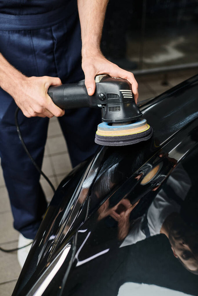 обрезанный вид преданного профессионального работника с помощью полировальной машины тщательно на черном автомобиле - Фото, изображение