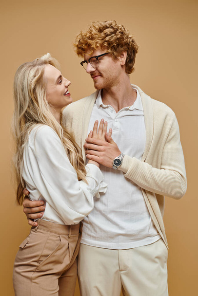 young stylish couple embracing and looking at each other on beige backdrop, old money style fashion - Photo, Image