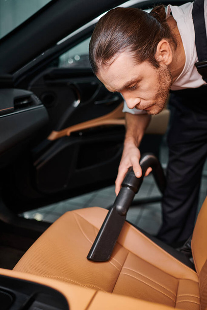 хорошо выглядящий трудолюбивый человек в форме с ручной уборкой в машине в гараже - Фото, изображение